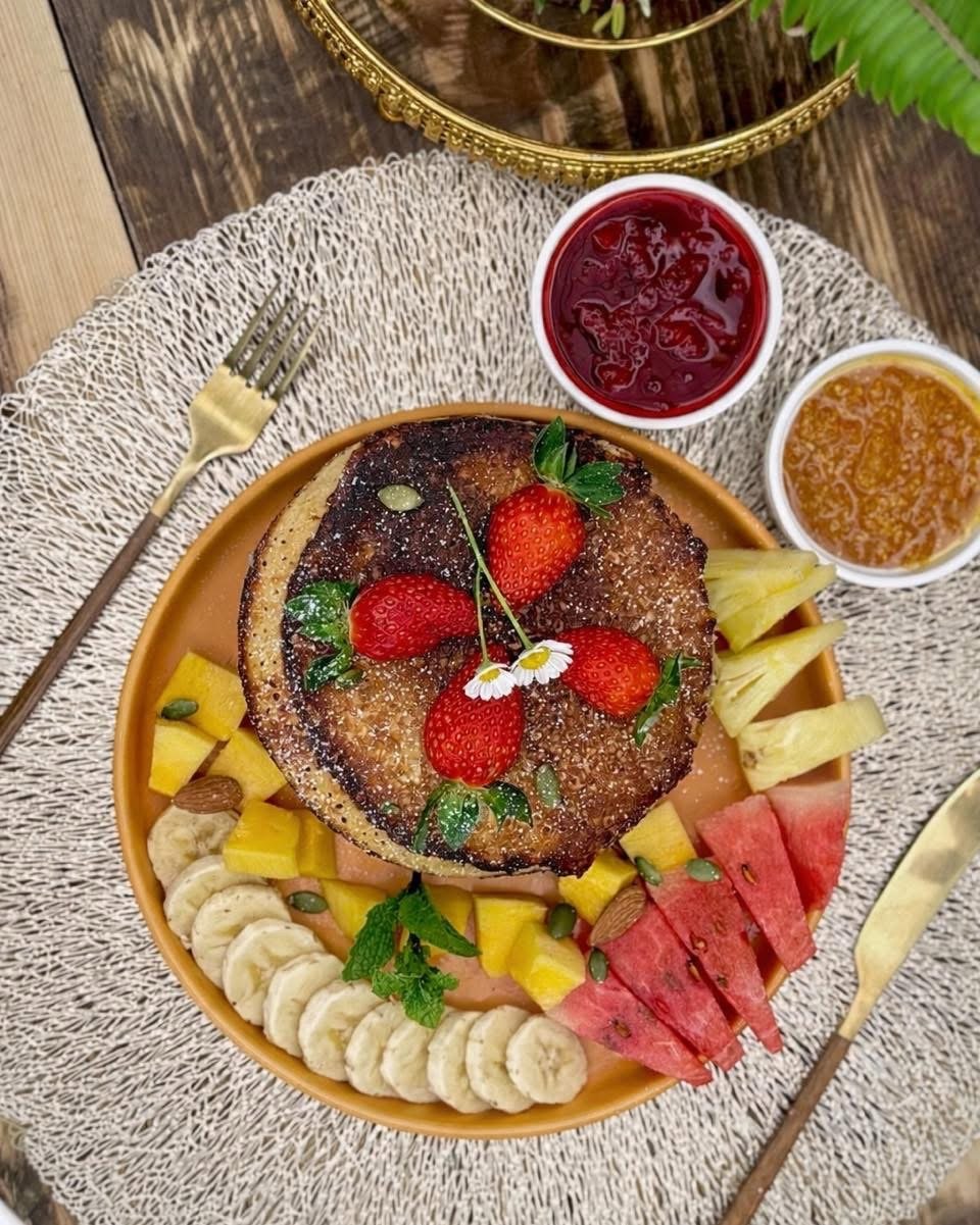 Pancakes with strawberries beside a platter of cut fruit