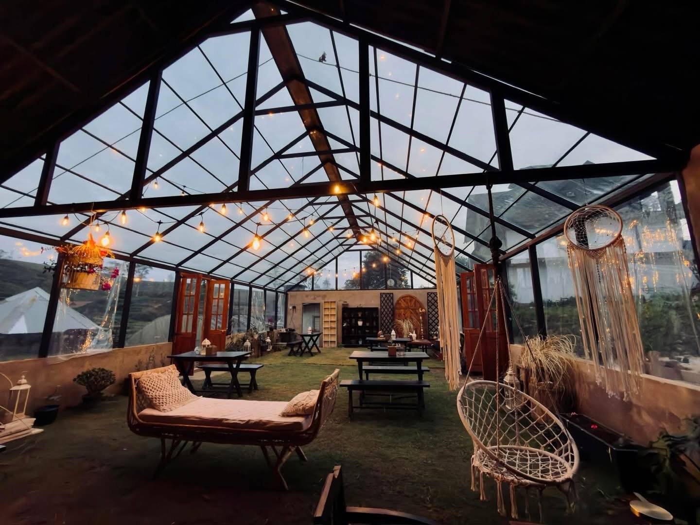 The greenhouse dining room at Forest Feast, with armchairs and long tables under the glass roof